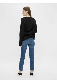Czarny sweter dziany z długimi rękawami, okrągłym dekoltem, w połączeniu z niebieskimi dżinsami o slim fit i tylnymi kieszeniami. W zestawie obuwie casualowe.