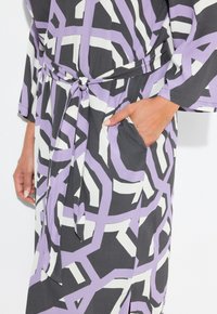 Abito lungo con un motivo geometrico viola, nero e bianco, dotato di vita legata e tasca laterale, realizzato in un tessuto leggero.