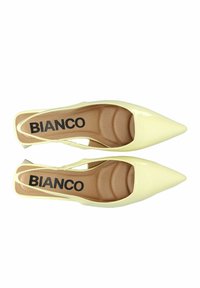 Keltaiset patenttireunuksiset slingback-korkokengät, joissa on terävä kärki, pitkät sisäpohjat ja musta "BIANCO"-logo pohjallisessa.
