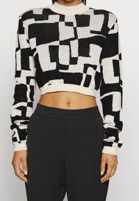 Zwart-witte cropped trui met een abstract geometrisch patroon. Gemaakt van gebreide stof met lange mouwen en een geribde halslijn.
