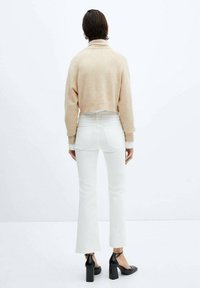 Maglione cropped beige, jeans bianchi a palazzo e scarpe con tacco nere. Texture lisce; design minimalista; il maglione presenta polsini a coste.