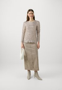 Top a maniche lunghe, aderente, in paillettes beige brillanti abbinato a una gonna di jeans alta vita beige. Gli accessori includono una borsa bianca e stivali alla caviglia grigi.