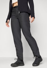 Svart utendørs bukser med teksturert overflate, glidelåslommer og slim-fit design, sammen med svarte tursko med teksturerte såler.