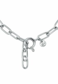 Collar de cadena de plata con eslabones alargados, un broche redondo y una pequeña etiqueta con dos piedras transparentes adheridas.