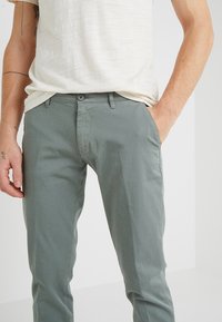 Pantaloni in cotone grigio chiaro da uomo con una texture liscia, dotati di chiusura con bottone, passanti per la cintura e tasche laterali.