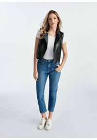 Czarna skórzana kamizelka na białym t-shircie, w połączeniu z jasnoniebieskimi dżinsami slim-fit i białymi trampkami. Gładka tekstura i dopasowany krój.