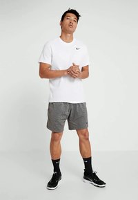 Biela tričko Nike, sivé športové šortky, čierne ponožky a čierne tenisky; tkanina je hladká, dizajn je jednoduchý, strih je voľný a športový.