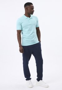 Polo shirt azzurro chiaro con maniche corte, abbinato a pantaloni blu navy e sneaker bianche. Tessuto liscio, design del colletto classico, branding minimal.