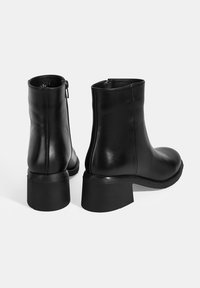 Bottes chevilles en cuir noir avec une texture lisse, fermeture par zip et un large talon block. Présente un design minimaliste avec un bout arrondi.