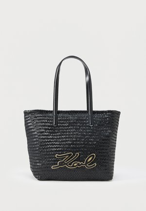Černá tkaná taška přes rameno s dvěma popruhy a zlatým logem „Karl“ na přední straně, na jednobílém pozadí.