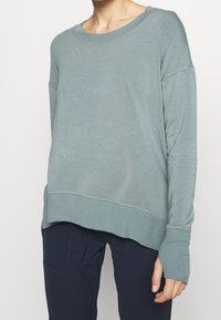 Felpa a maniche lunghe di un blu verde chiaro con una vestibilità rilassata, scollatura rotonda e polsini a coste. Presenta dettagli di cucitura sottili.