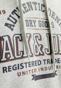 Grauer Kapuzenpullover mit gedrucktem Text in Dunkelblau und Kastanienbraun, ausgestattet mit einem Kordelzug und einem strukturierten Stoff. Details umfassen Marken- und Qualitätsindikatoren.