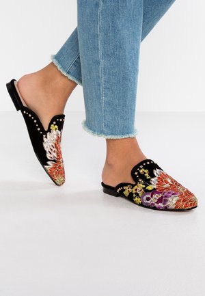 Stopy w czarnych wsuwanych butach ozdobionych kolorowym haftem kwiatowym i małymi złotymi ćwiekami, zestawione z jasnoniebieskimi dżinsami z postrzępionymi nogawkami.