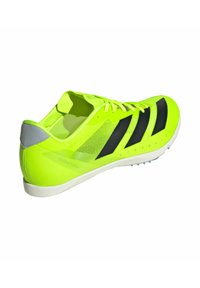 Zapatilla deportiva verde con parte superior de malla ligera, acentos negros y suela blanca. Presenta un talón reforzado y suela con clavos para mayor tracción.