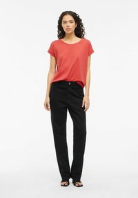 T-shirt rosso a maniche corte abbinato a jeans neri dritti. L'outfit presenta un design semplice e un tessuto traspirante, con dettagli minimi.