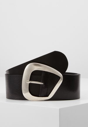 Zwarte leren riem met een grote, onregelmatige zilveren gesp, opgerold en geplaatst op een wit oppervlak tegen een effen achtergrond.