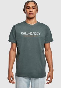 Camiseta de algodón verde oscuro con cuello redondo. Presenta texto en blanco y naranja: "OFICINAS DE PARENTALIDAD CALL of DADDY". Manga corta, corte relajado.