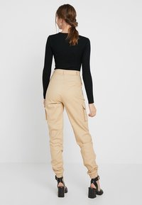 Beige cargobyxor med avsmalnande anklar, sidofickor och hög midja, tillsammans med en svart figurnära ribbad topp, sedd bakifrån.