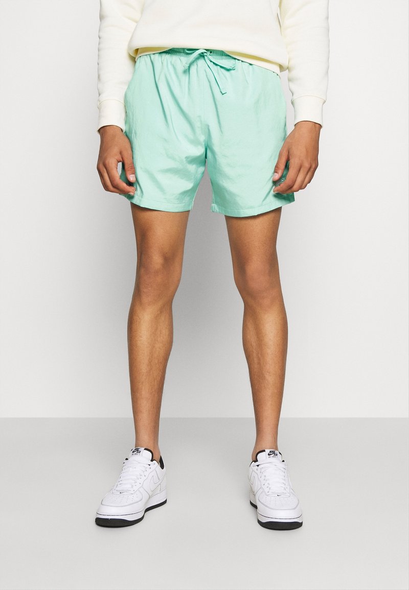 Shorts de bain vert menthe clair en tissu à séchage rapide, dotés d'une taille élastique avec cordon de serrage et de poches latérales.