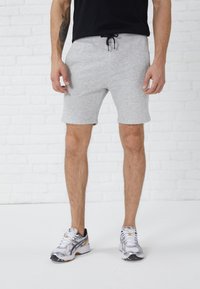 Lyse grå treningshorts laget av bomullsblanding, med elastisk midje, snor og side lommer. Brukt med sølvfargede joggesko.