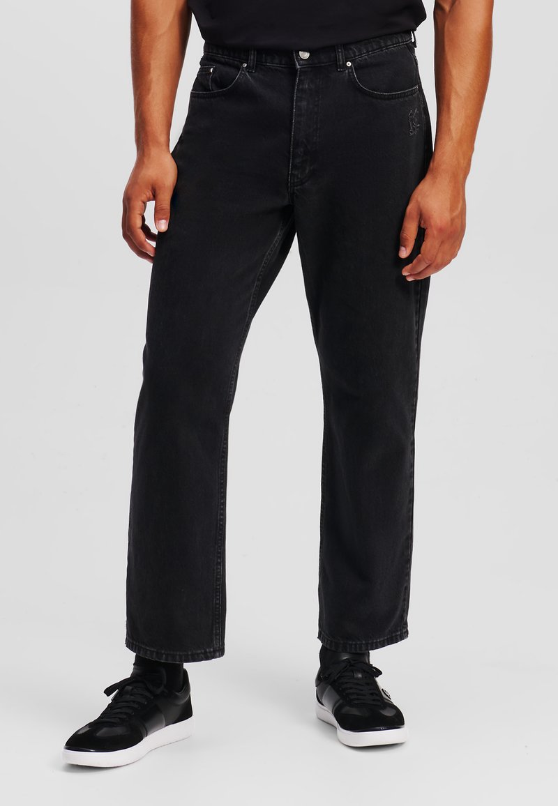 Vaqueros de mezclilla negra con un corte recto, que cuentan con cinco bolsillos y sutiles acentos de costura. Combinados con zapatillas negras.