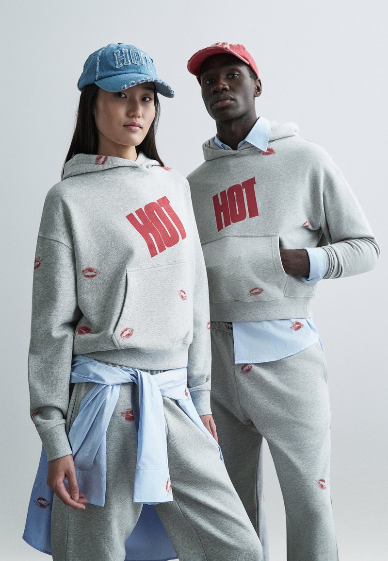 Grå huvtröjor med röd "HOT"-tryck, prydda med läpptryck. Blå denim och röda kepsar, med en ljusblå skjorta under.