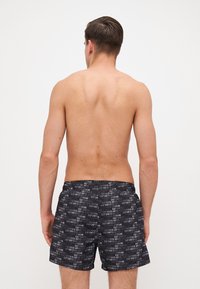 Fekete úszónadrág, amelyet az "Emporio Armani" logó ismétlődő mintázata díszít. Könnyű anyagból készült, rugalmas derékrésszel és oldalsó zsebekkel.