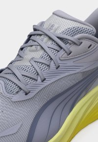 Κοντινό πλάνο αθλητικού παπουτσιού ανοιχτού γκρι με υφασμάτινη υφή, γκρι κορδόνια και κίτρινη ενισχυμένη σόλα.