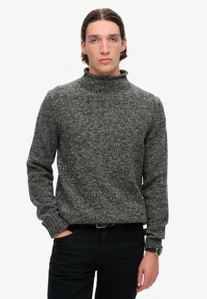 Zwart-wit gemêleerd turtleneck-trui met lange mouwen, ontspannen pasvorm en geribbelde manchetten. Gedragen met zwarte broek en polshorloge.