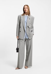 Γκρι σακάκι διπλού στήθους με μαύρα κουμπιά, σε συνδυασμό με ανοιχτό μπλε πουκάμισο με ρίγες, γκρι παντελόνι με φαρδιά μπατζάκια και μπεζ γόβες με μυτερή μύτη.