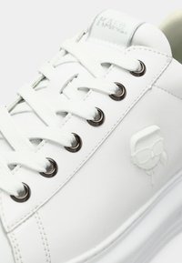 Sapatilha branca em couro com atacadores tonais e ilhós metálicos. Apresenta detalhe de logótipo em relevo no lado exterior e colarinho almofadado.