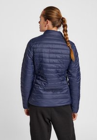 Giacca a vento blu navy con cuciture orizzontali; materiale leggero e resistente all'acqua; colletto alto; design aderente; vista posteriore.