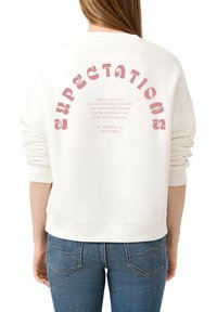 Crème sweatshirt met een gebogen roze tekstgrafiek op de achterkant, met motiverende zinnen gecentreerd onder "VERWACHTINGEN." Zachte katoenen stof.