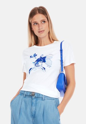White cotton t-shirt featuring a blue fish graphic. Paired with light blue denim pants and a small blue shoulder bag.