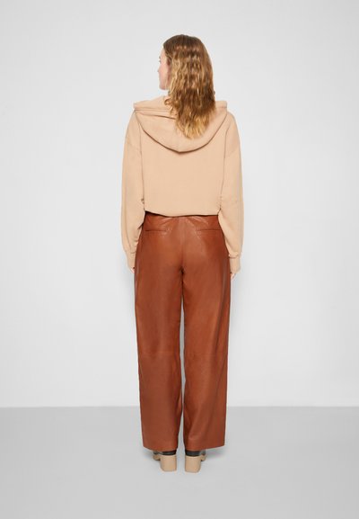 Sweatshirt bege com capuz e corte descontraído, combinado com calças largas de couro castanho e sapatos plataforma bege, visto de costas.