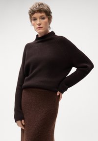 Maglione marrone a coste con colletto alto, abbinato a una gonna fuzzy marrone lunga fino al ginocchio. La trama del tessuto appare morbida e calda.