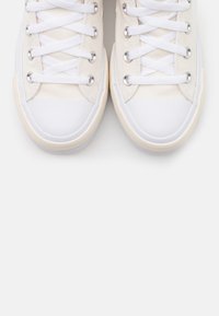 Para off-white sneakersów z płótna z białymi gumowymi czubkami i białymi sznurówkami na jasnoszarym tle.