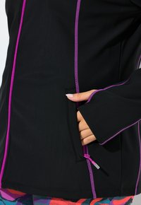 Sort jakke med lilla lynlås og detaljer; lavet af glat, let materiale; har en sidelomme og lange ærmer.