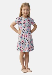 Blumenkleid aus leichtem Stoff, mit rosa, blauen und schwarzen Mustern, kurzen Ärmeln und einem schwingenden Rock. Die Schuhe sind beige Ballerinas.