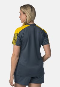 Maglietta sportiva grigia con accenti gialli. Presenta motivi testurizzati su spalle e maniche. Design leggero e aderente per l'abbigliamento attivo.