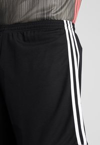 Mustat urheilushortsit, joissa on valkoiset sivuraidat, valmistettu kevyestä kankaasta. Sisältää joustavan vyötärön mukavuutta varten.