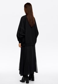Sudadera negra oversized con mangas texturizadas, combinada con una fluida falda larga negra. Botines negros con detalles sutiles.
