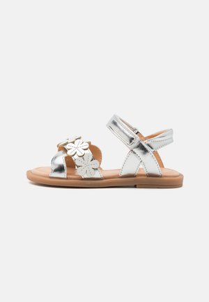 Silver metallic sandals with floral accents, open toe design, adjustable ankle strap, and tan textured footbed. Flat sole.