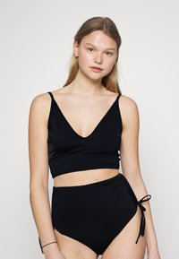 Conjunto de biquíni preto com um top cropped de decote em V e parte de baixo de cintura alta. O top tem alças finas e a parte de baixo inclui laços laterais ajustáveis. Textura suave.