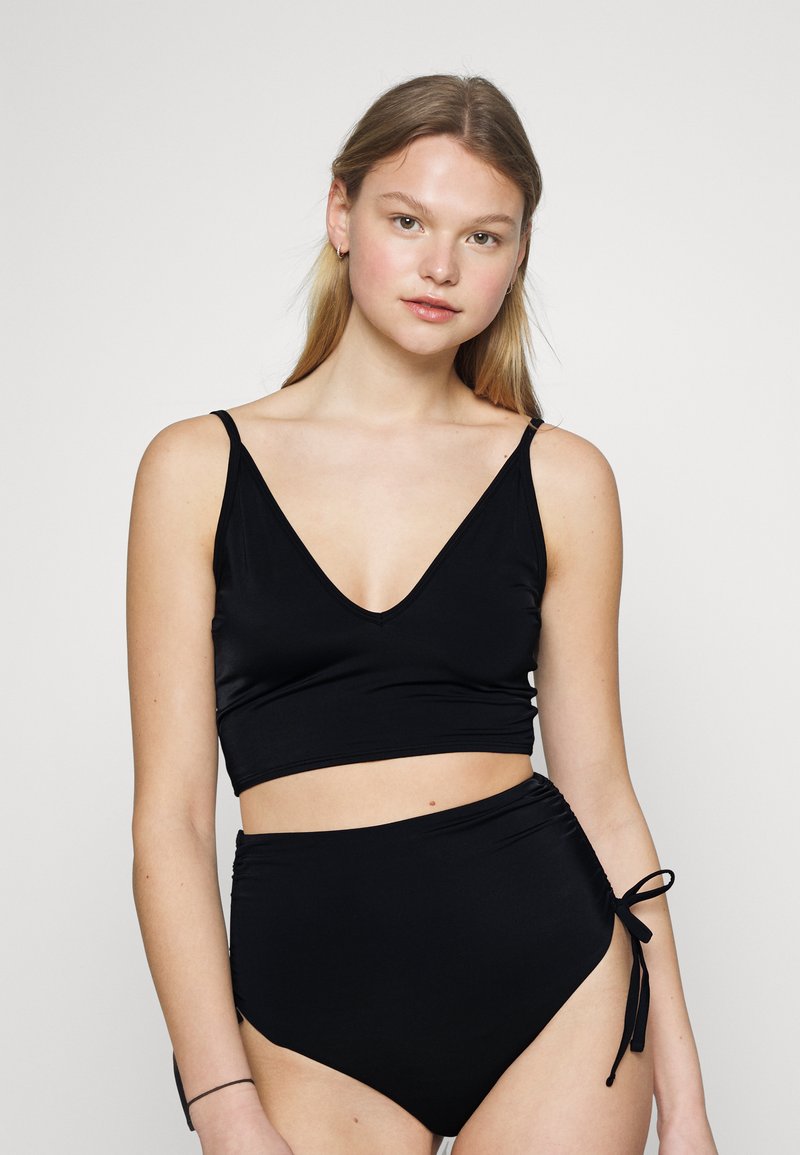Conjunto de biquíni preto com um top cropped de decote em V e parte de baixo de cintura alta. O top tem alças finas e a parte de baixo inclui laços laterais ajustáveis. Textura suave.