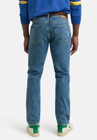 Blå denimjeans med rett benklipp, baklommer og detaljer i brunt skinn rundt livet. Kombinert med grønne og hvite joggesko.