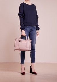 Sudadera marina con mangas acampanadas, combinada con jeans ajustados azul, un bolso rosa claro y zapatos de tacón burdeos.