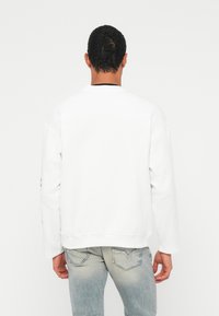 Felpa bianca con maniche lunghe e polsini a costine, con scollo rotondo e orlo dritto, abbinata a jeans in denim chiaro.