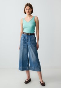 Débardeur bleu clair à côtes, culottes en denim taille haute et large, ceinture en cuir marron, et ballerines à brides décoratives noires.