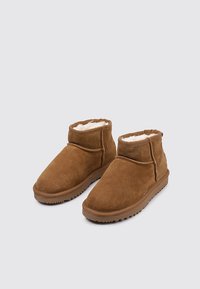 Botines de ante marrón con un forro interior suave y suela de goma, que presentan un diseño de altura media y detalles cosidos a lo largo de las costuras.